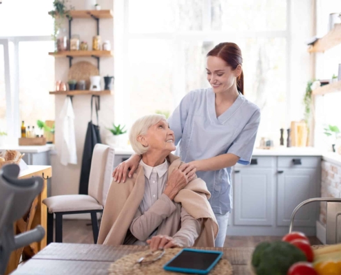 Front view of an elder sitting down and smiling up at her caregiver