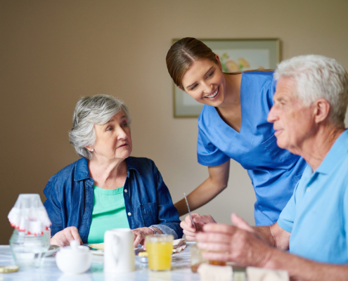 Nurse Checking In On Couple In Assisted Living Dining Room
