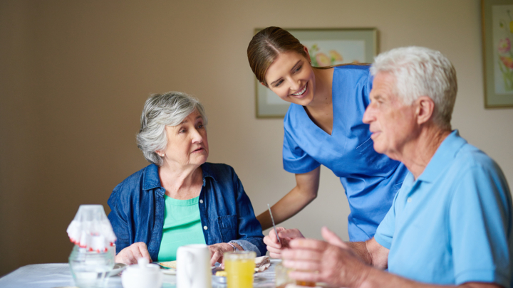 Nurse Checking In On Couple In Assisted Living Dining Room