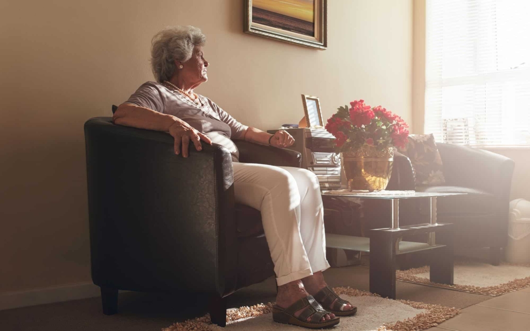 Side view of an elderly woman sitting in a chair looking out of the window