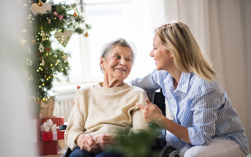 A Senior Woman In Wheelchair With A Health Visitor At Home At Christmas Time
