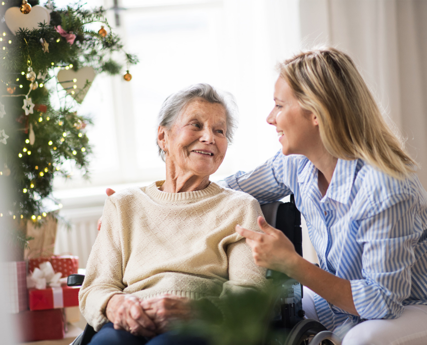 A Senior Woman In Wheelchair With A Health Visitor At Home At Christmas Time