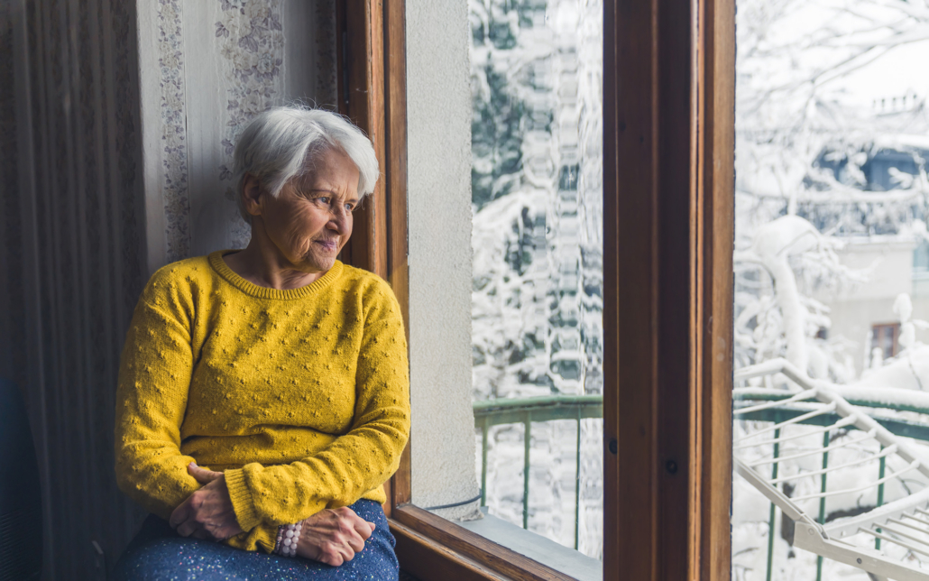 Elderly Person Sitting At Window Looking At Snow