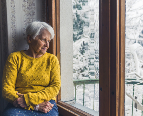 Elderly Person Sitting At Window Looking At Snow
