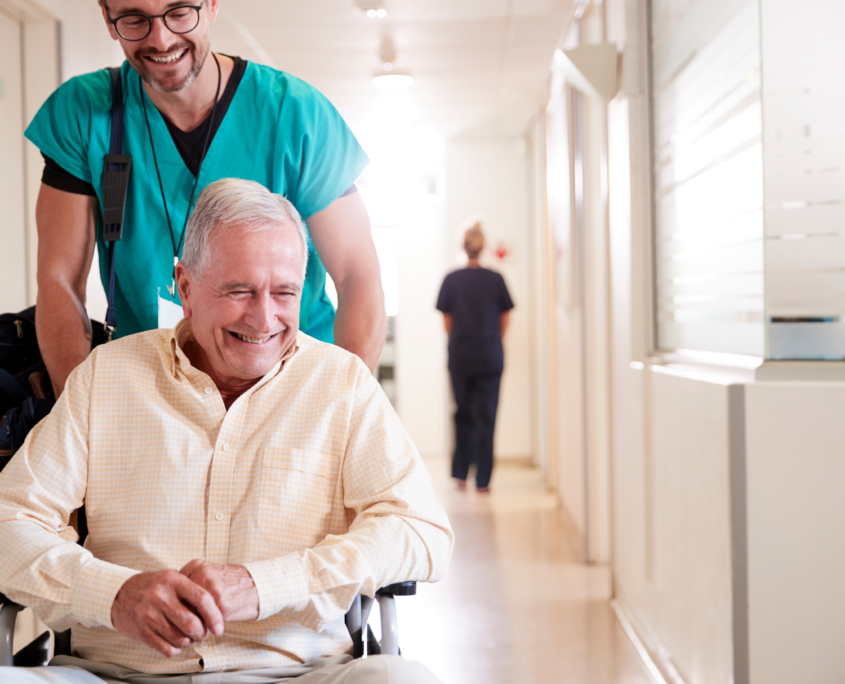 Male Orderly Pushing Senior Male Patient Being Discharged From Hospital In Wheelchair